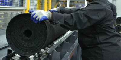 A factory worker handling a large roll of rubber product 